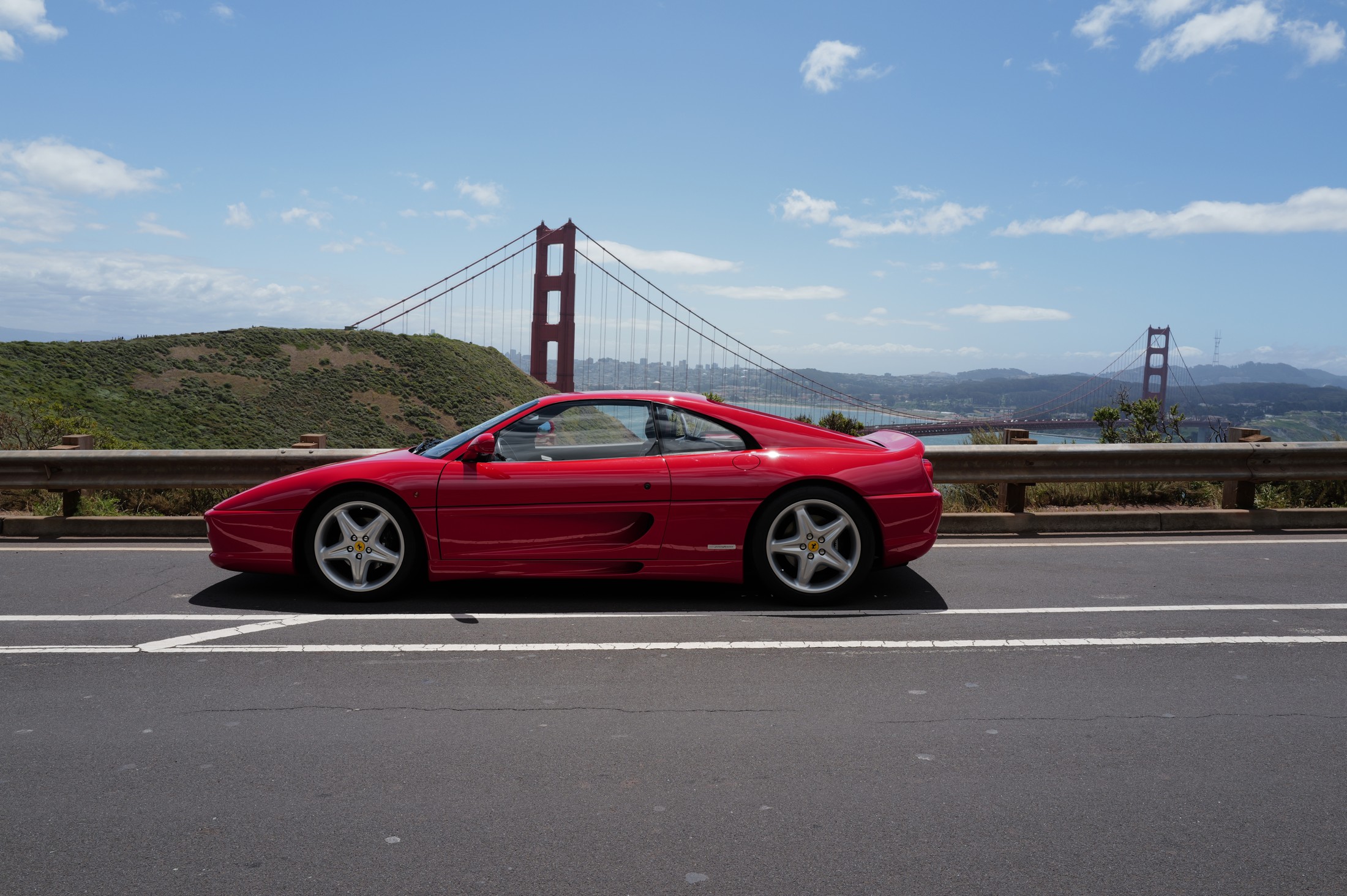 Red Ferrari F355 in side profile with the Golden Gate Bridge in the background